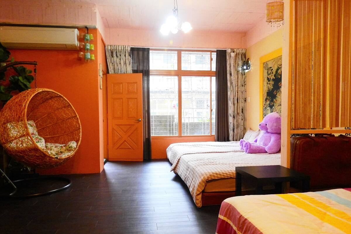 A bedroom with two beds, a hanging chair, a window with curtains, and a wall-mounted lamp.