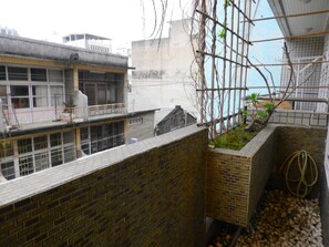 A view of a building with a brick wall and a balcony. There is a garden area with plants and a hose. - House 123 Lan (Tainan)