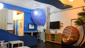 A room with a blue accent wall, a striped bed, a television, a decorative hanging chair, and a small table. - House 123 Lan (Tainan)