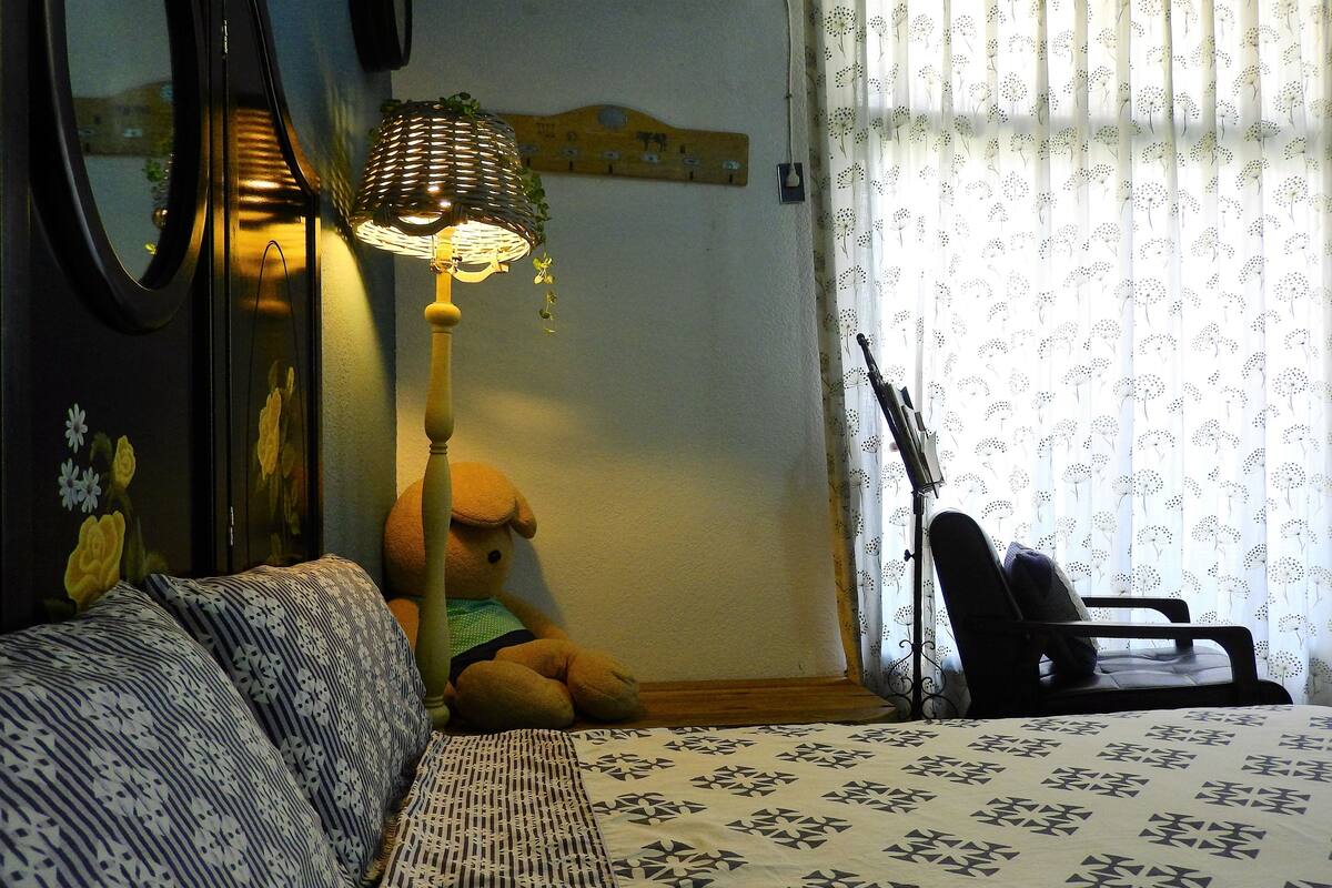 A room with a bed, a lamp, a teddy bear, and a guitar.