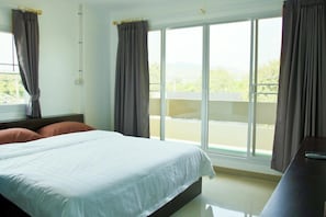 A hotel room with a large bed, two windows with curtains, a view of a balcony, and a desk with a remote control. - U Dee Room & Coffee (Kanchanaburi)