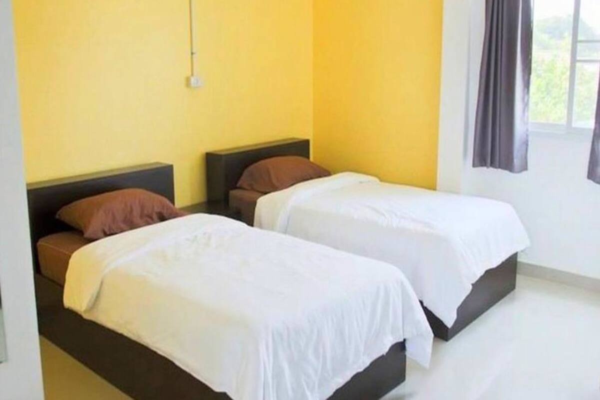 A hotel room with two single beds, a window with curtains, and a yellow wall.
