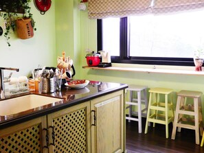 A kitchen with a wooden countertop, a sink, and a window with a view. There are stools and a red pot on the counter. - Anping Western-style House (Tainan)