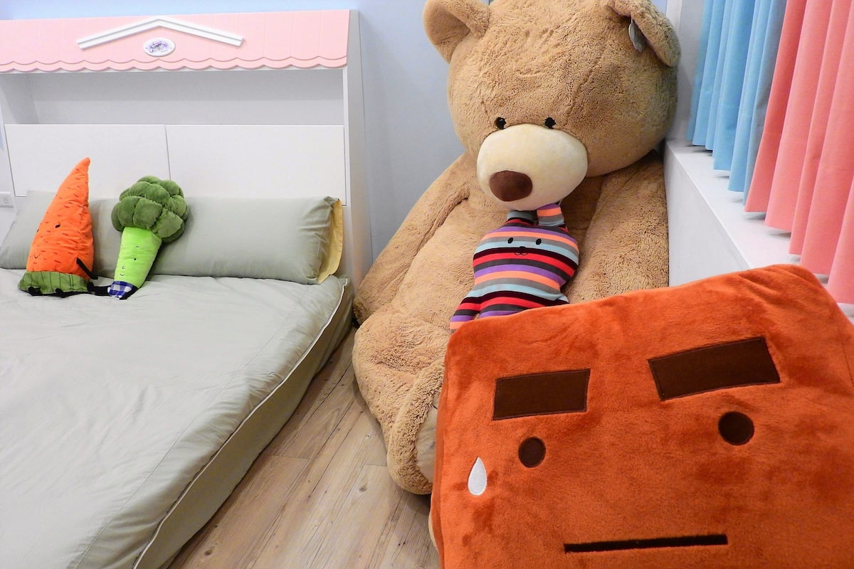 A room with a bed, a large teddy bear, and a plush carrot.