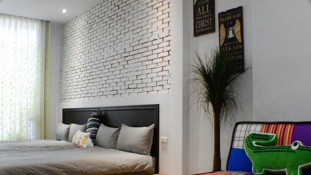 A bedroom with a brick-patterned headboard, a bed with pillows, a nightstand, and a colorful sofa with a crocodile decoration.