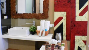 A bathroom with a white sink, a mirror with a stone frame, a towel rack, and a red and white wall decoration.