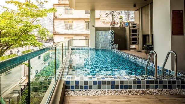 A swimming pool with a tiled floor, a glass railing, and a view of the street and buildings in the background. - Casa Asara (Bangkok)