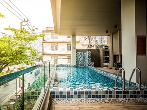 A swimming pool with a tiled floor, a glass railing, and a view of the street and buildings in the background. - Casa Asara (Bangkok)