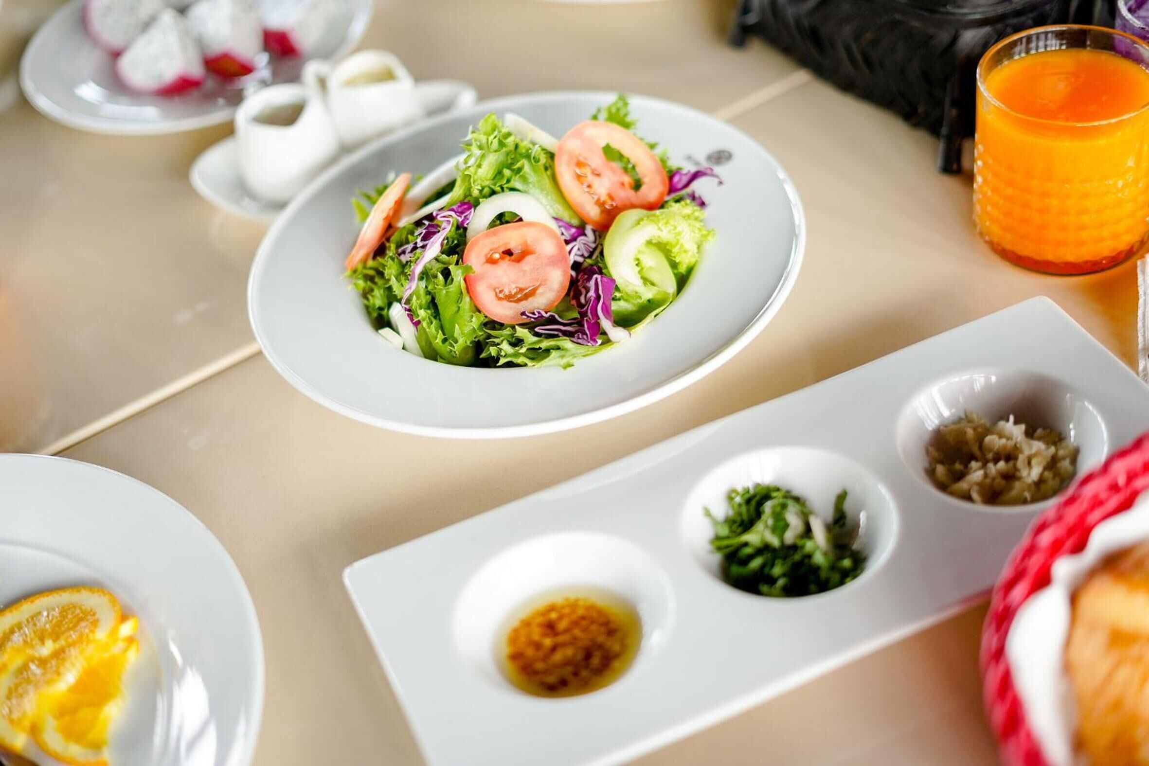 A dining table with a plate of salad, two small bowls of condiments, and a glass of orange juice.