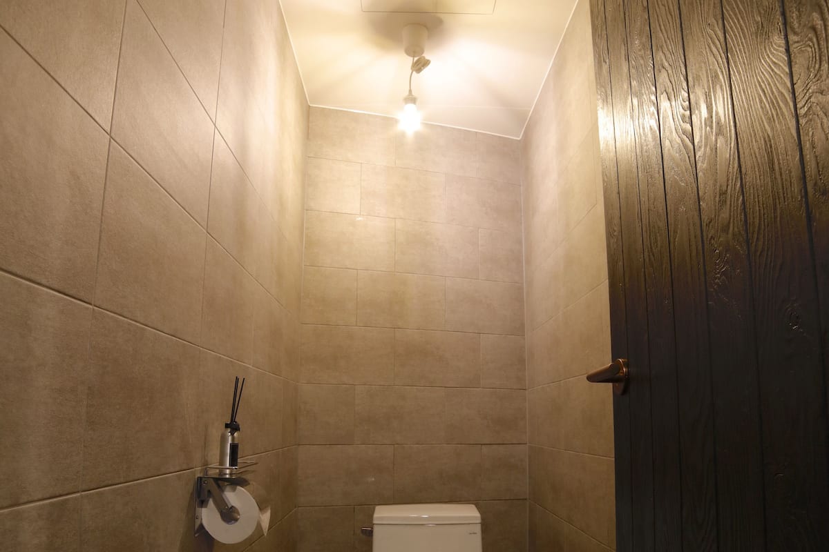 A small, tiled bathroom with a toilet, a trash can, and a wooden door.
