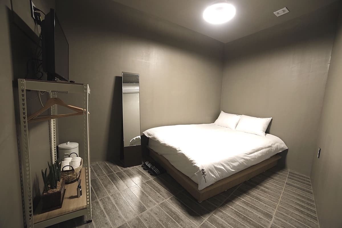 A bedroom with a bed, a wardrobe, a mirror, and a small table with a plant and a candle.