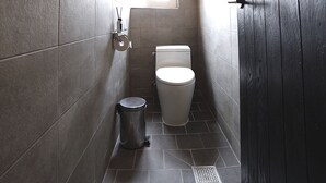 A narrow bathroom with a toilet, a trash bin, and a window. - The Bay Guesthouse - Hostel (Busan)