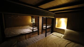 A dormitory-style room with bunk beds, a small table, and a window with a light fixture.