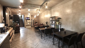 A modern interior with a herringbone floor, wooden tables, black chairs, and a staircase leading to another level. - The Bay Guesthouse - Hostel (Busan)