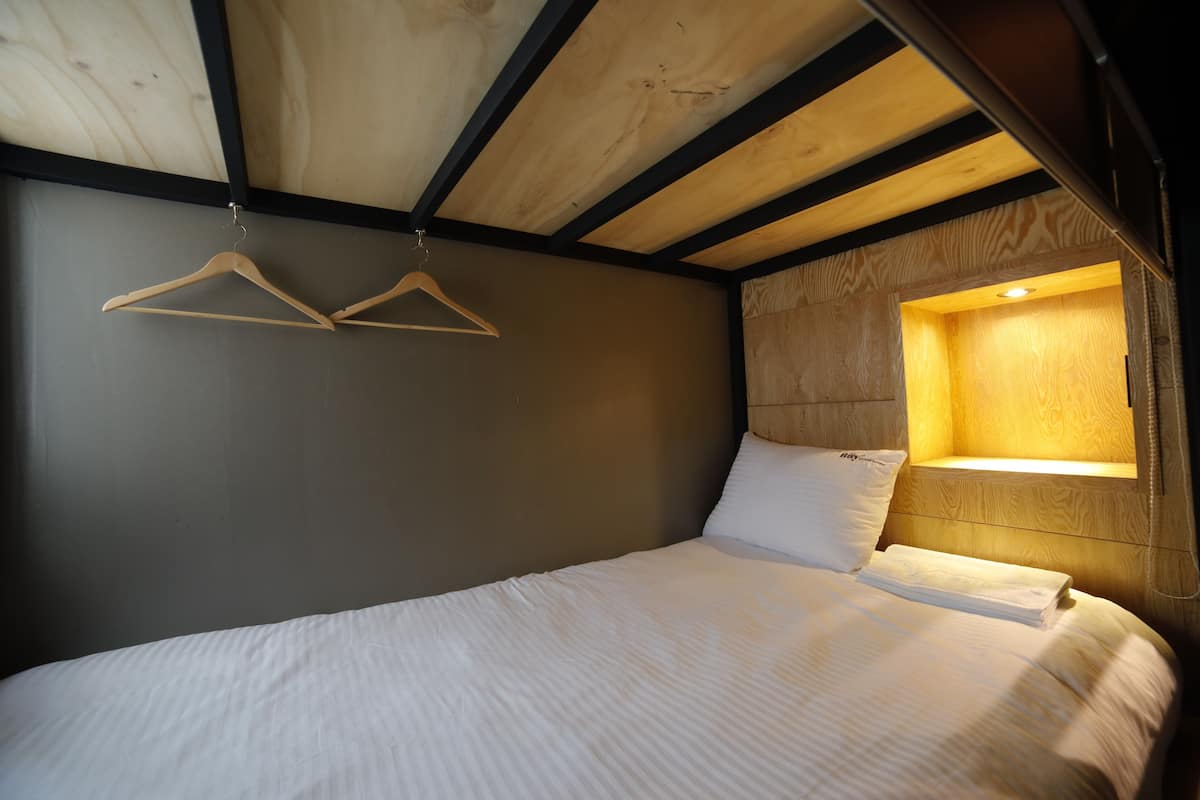 A bedroom with a wooden ceiling, a bed with white bedding, and a bedside table with a lamp.