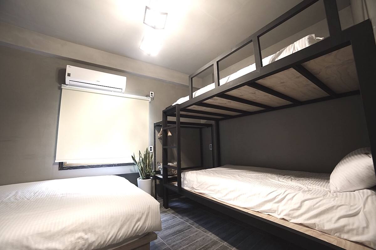 A room with bunk beds, a window with blinds, an air conditioning unit, and a potted plant.