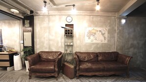 A room with two brown leather sofas, a wooden cabinet, a globe map on the wall, and a clock. - The Bay Guesthouse - Hostel (Busan)