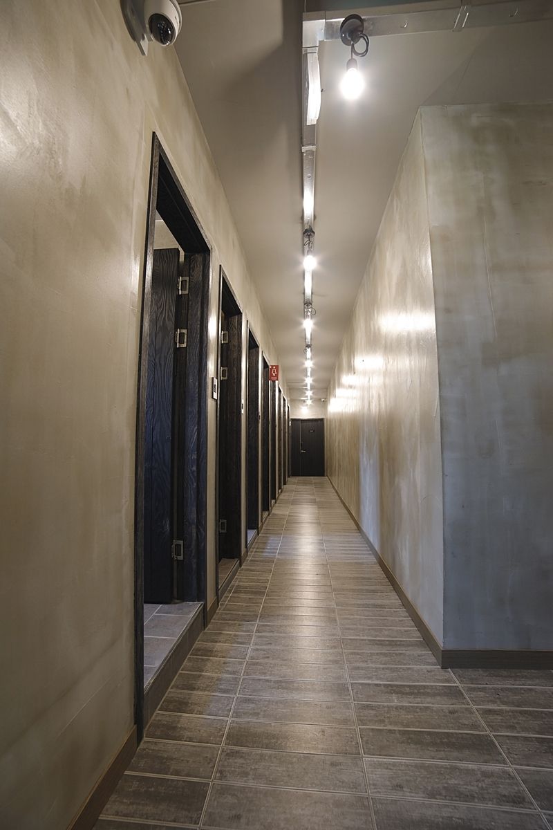 A long, narrow hallway with doors on one side and a plain wall on the other, with a ceiling light fixture running along the length.