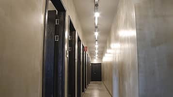 A long, narrow hallway with doors on one side and a plain wall on the other, with a ceiling light fixture running along the length.
