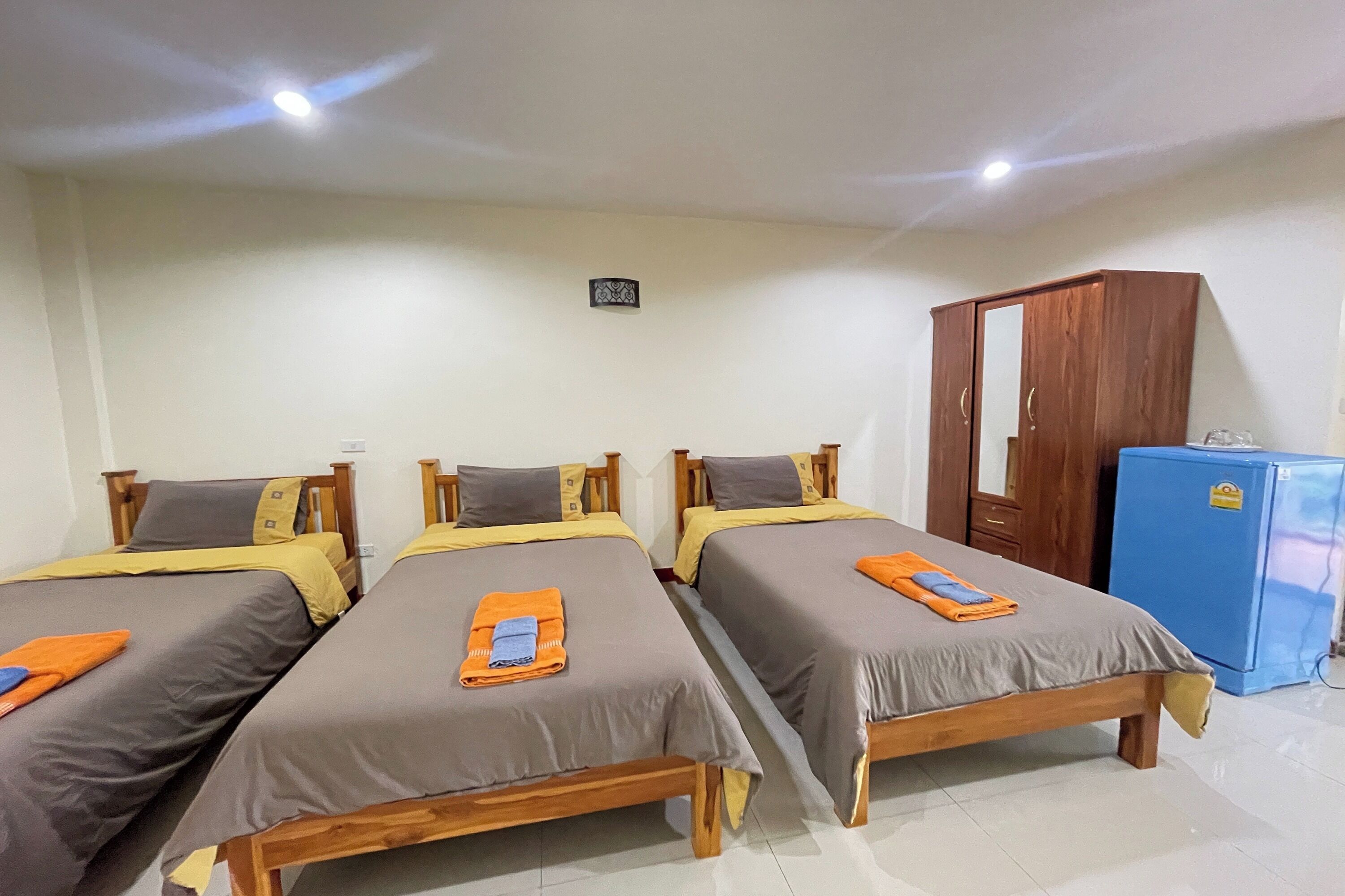 A room with three wooden beds, each with a grey and yellow bedspread, and a blue refrigerator.
