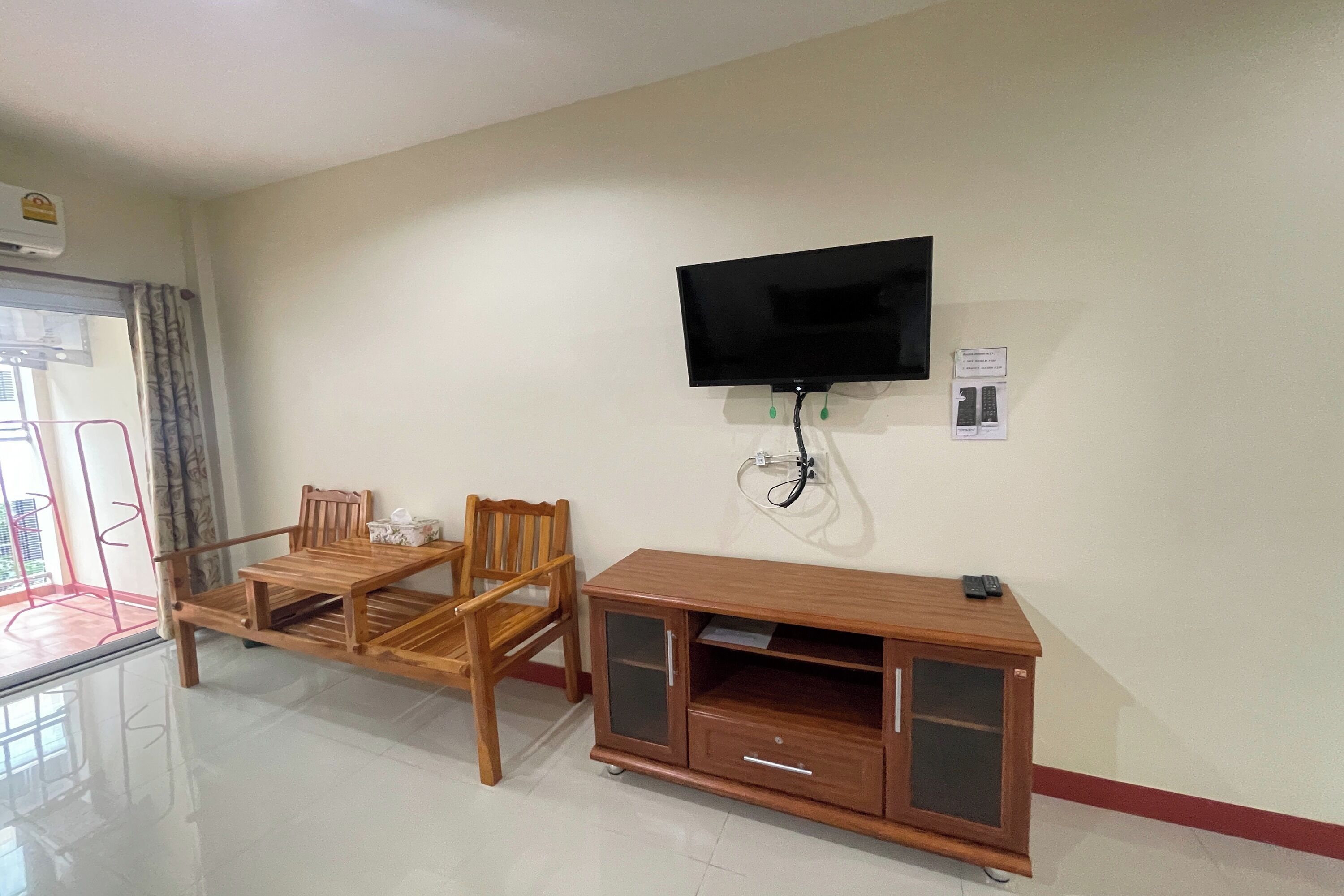 A room with a wooden dining table and chairs, a wooden cabinet with drawers, a mounted television, and a window with curtains.