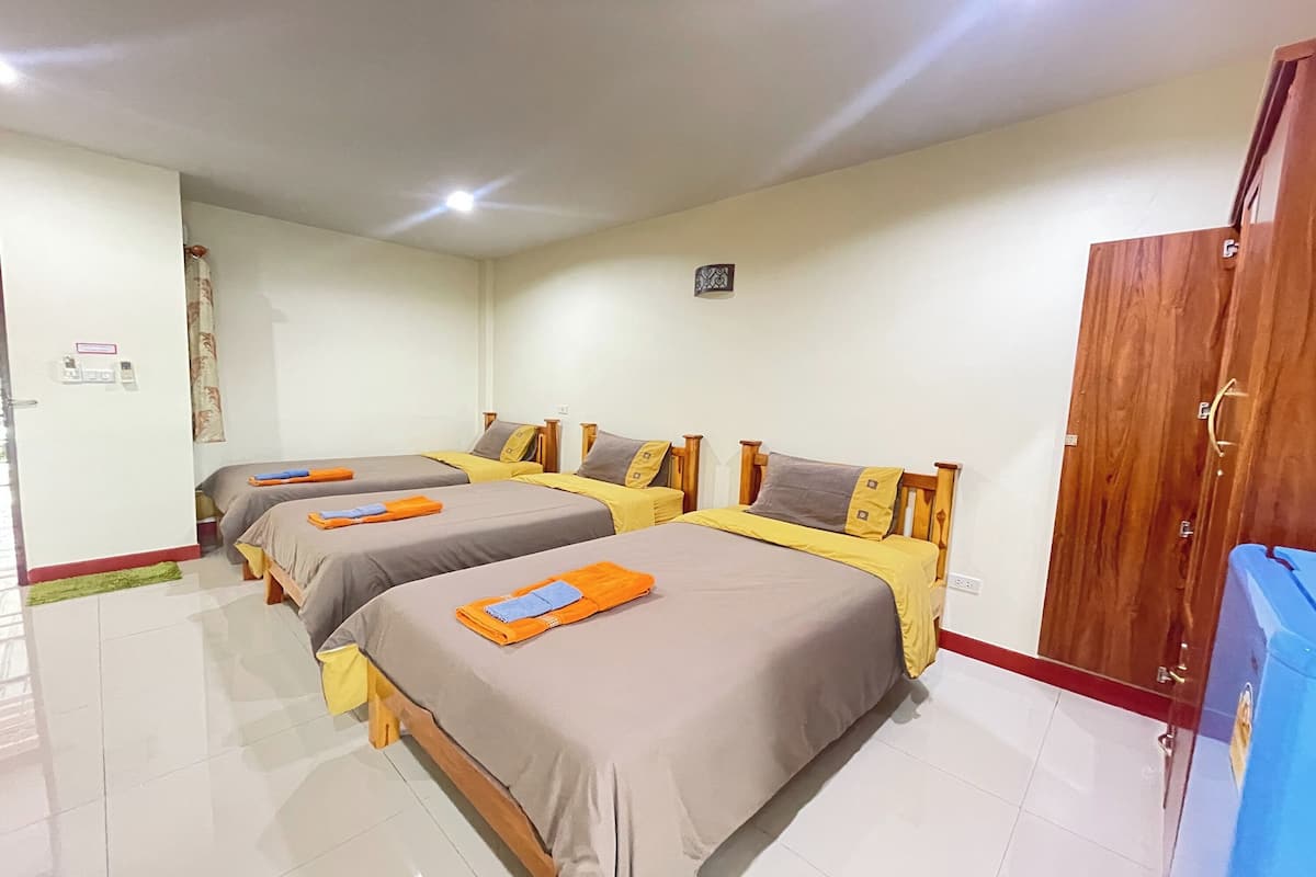 Habitación de hotel con tres camas, cabeceros de madera y un armario.