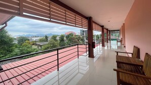 A corridor with a red-roofed outdoor area, wooden benches, and a view of buildings and greenery. - P&P Place (Kanchanaburi)