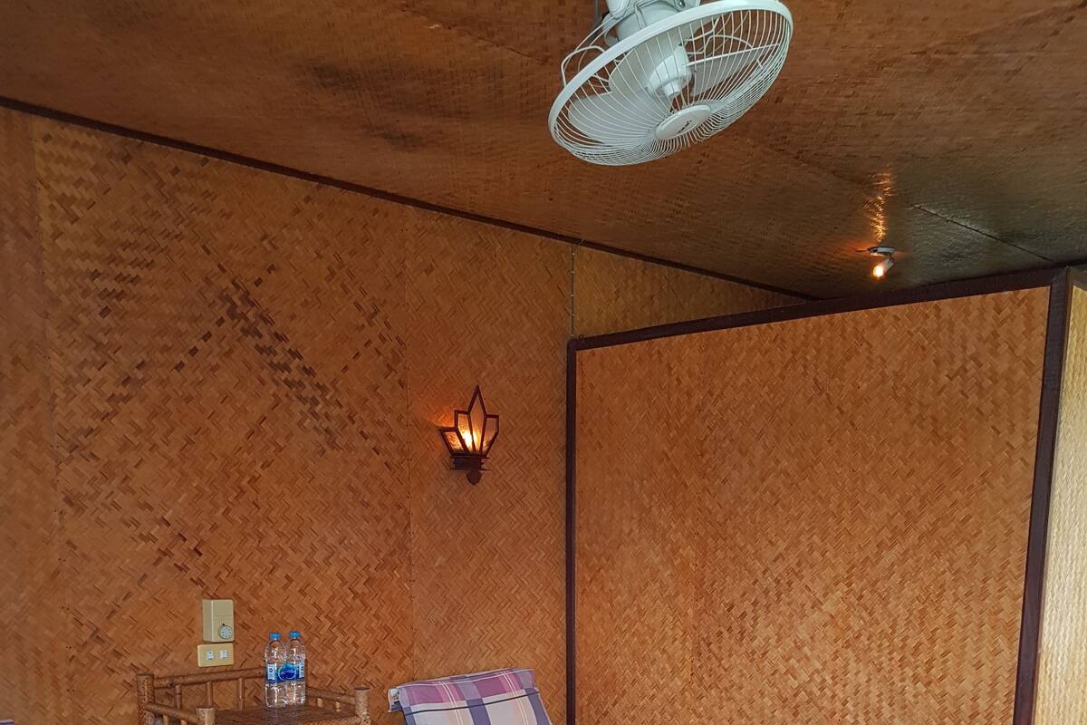 A room with two beds, a wooden headboard, a wall-mounted light fixture, and a ceiling fan.