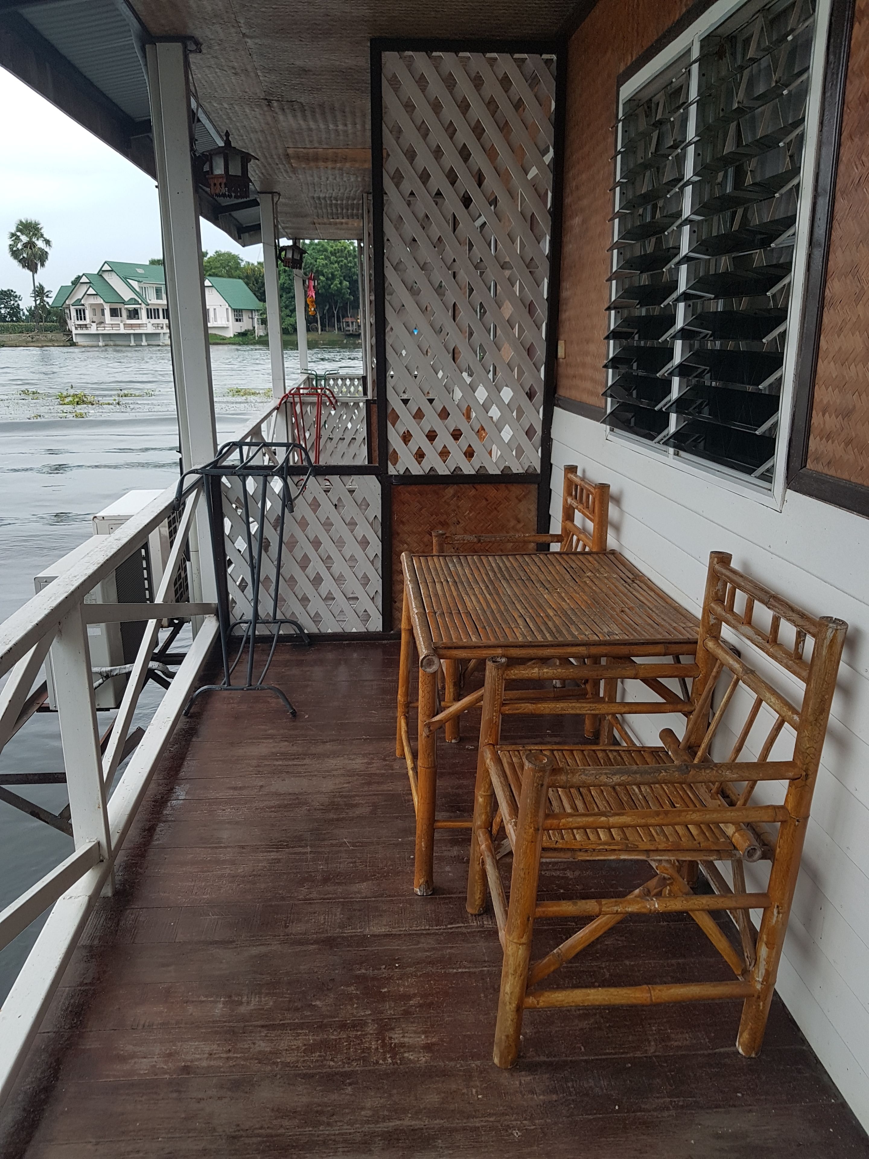 A wooden table and chairs on a covered porch with a view of a river and houses in the background.