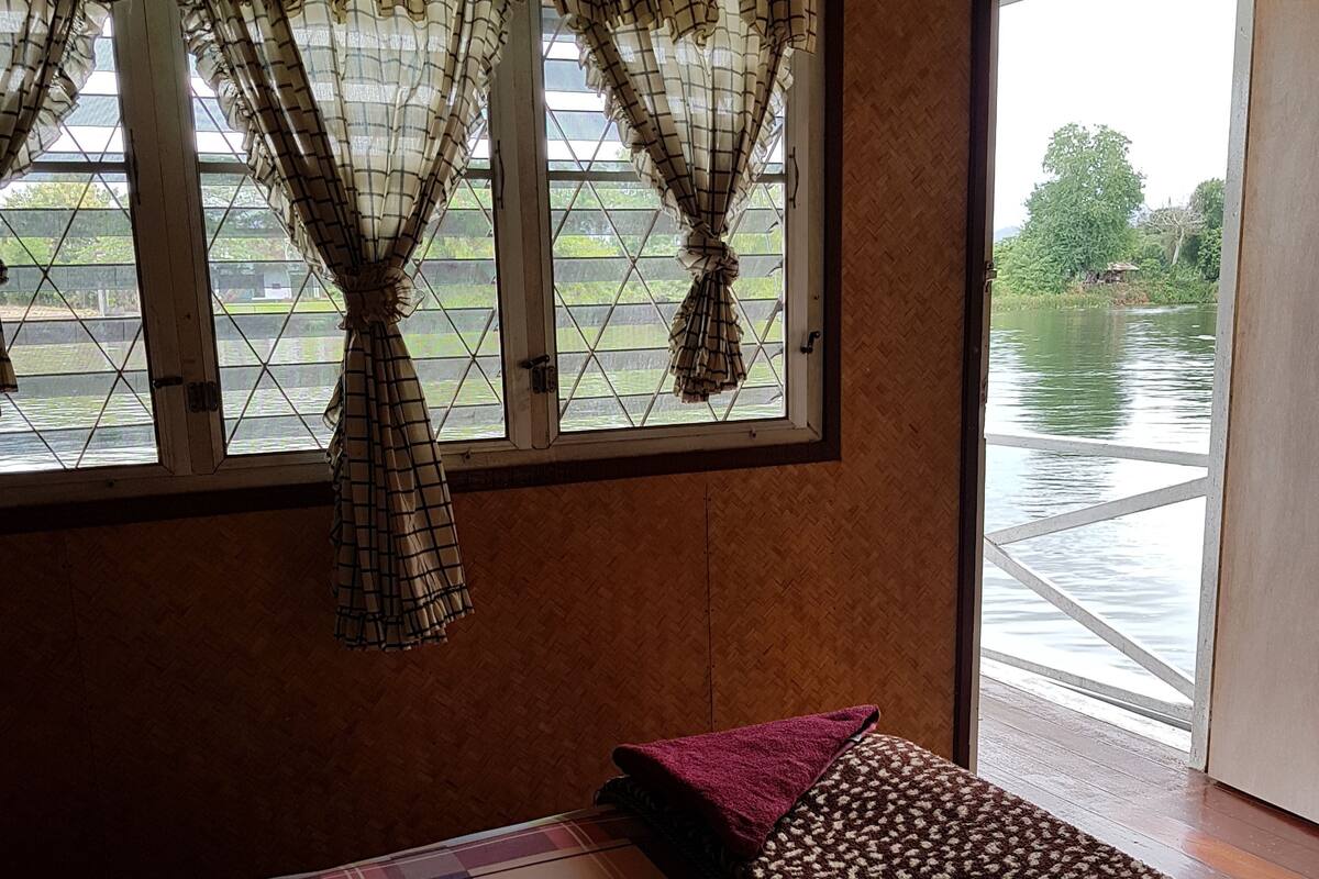 A room with a window, a bed with a colorful bedspread, and a view of a water body outside.