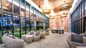 Ein moderner Lounge-Bereich mit Korbmöbeln, großen Fenstern und Holzdekor an der Decke.