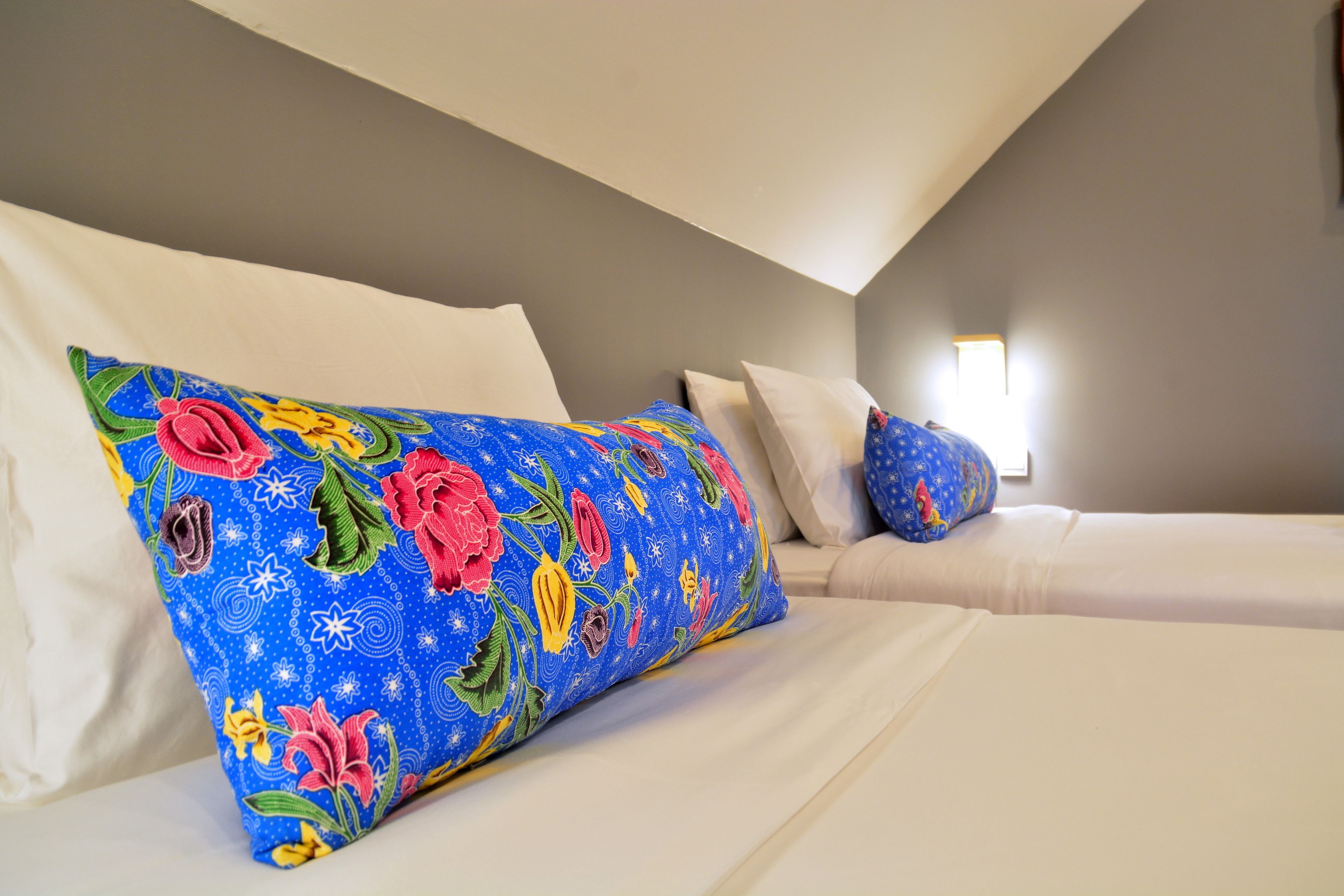 Quarto de hotel com cama, roupa de cama branca e almofada estampada com flores.