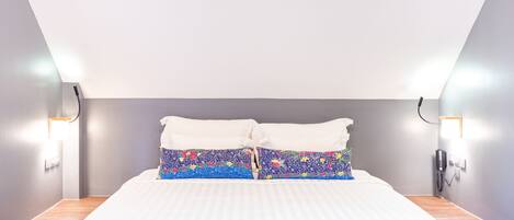 A neatly made bed with white linens and a colorful floral pillow.
