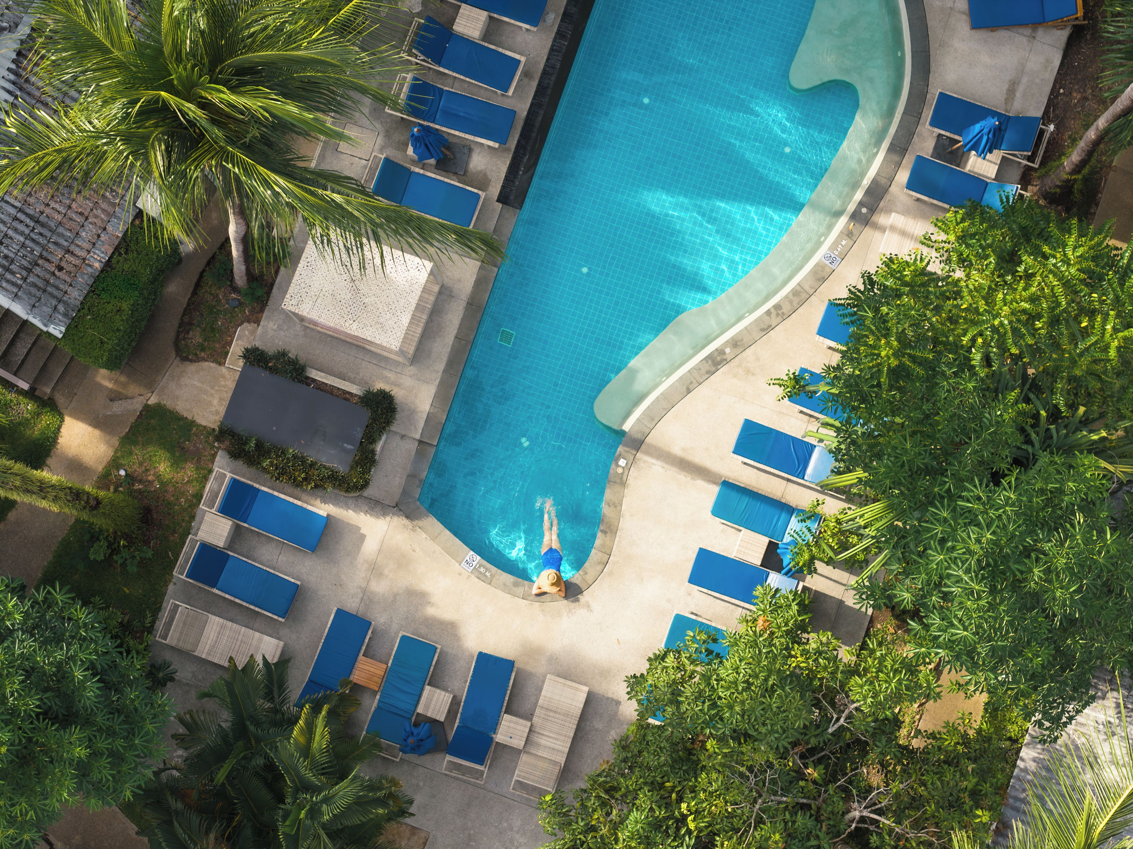 An aerial view of a swimming pool with lounge chairs and palm trees.