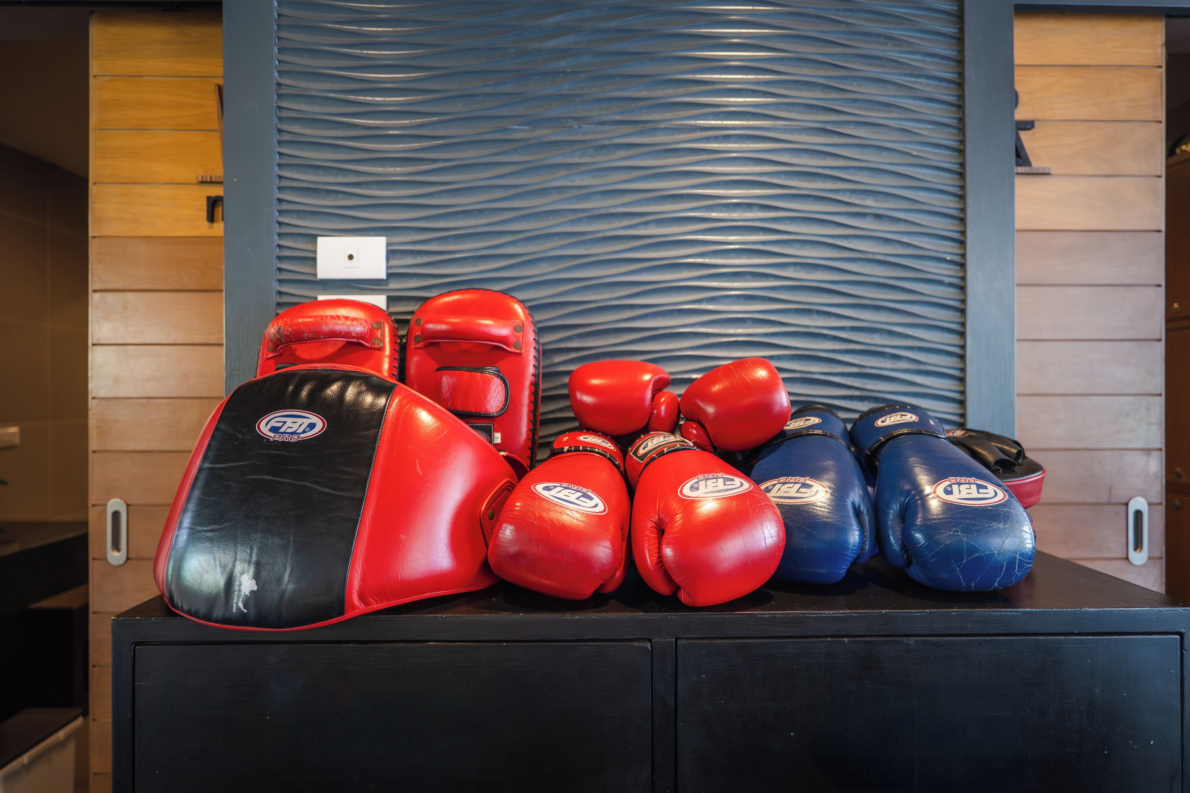 Eine Sammlung von Boxhandschuhen auf einer schwarzen Oberfläche, im Hintergrund eine strukturierte Wand.