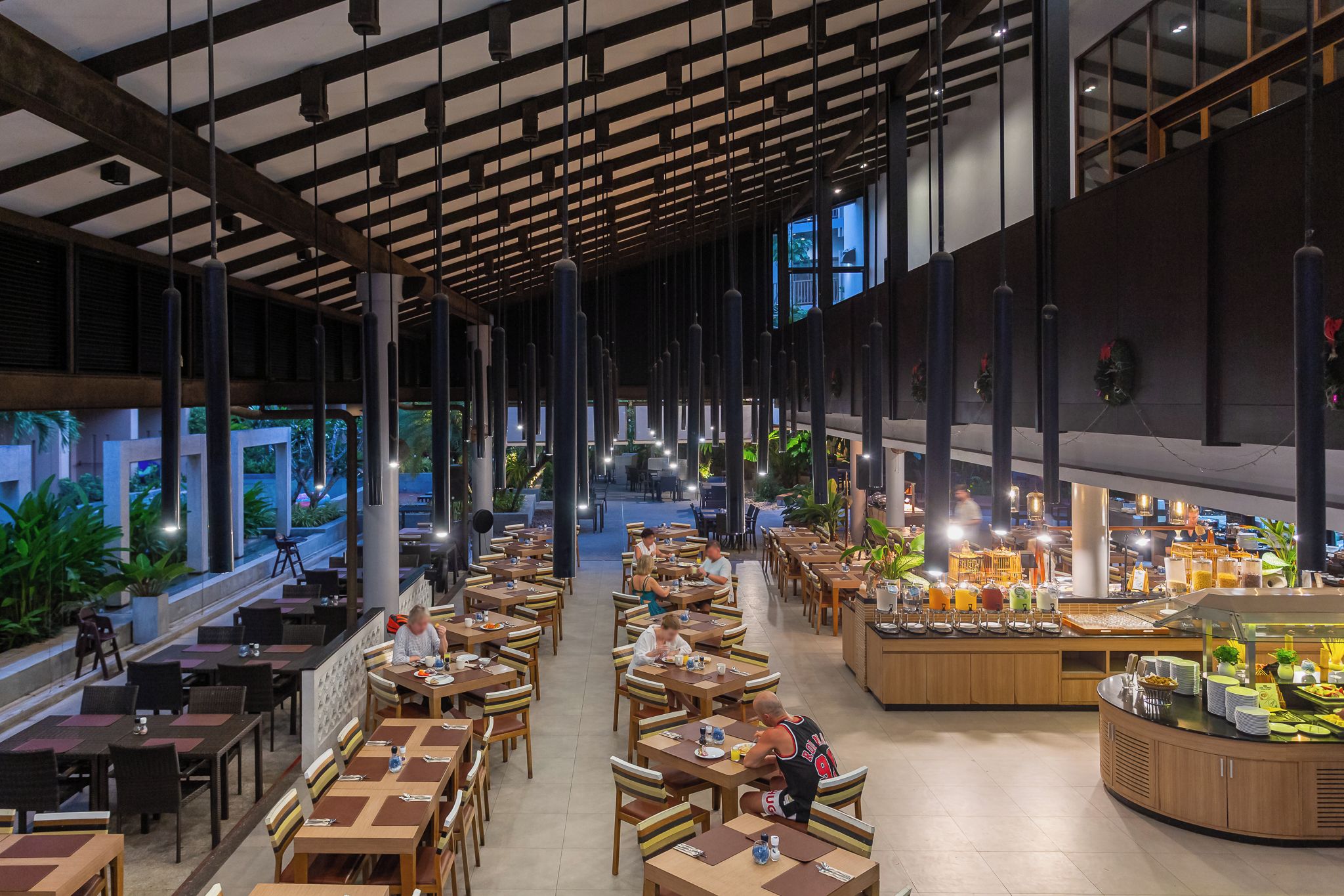 Un amplio comedor interior con varias mesas y sillas, una barra de buffet con diferentes opciones de comida, y ventanas grandes que dejan entrar luz natural.