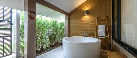 Un baño moderno con una bañera grande, un banco de madera y vistas a la vegetación exterior.