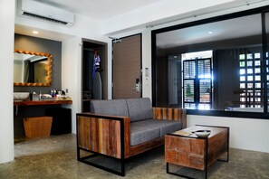 A modern living room with a grey sofa, a wooden coffee table, a small side table, a built-in bench, a large mirror, a wooden cabinet, and a window with blinds. - Deevana Krabi Resort (Krabi)