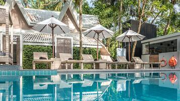 Un espace piscine agrémenté de chaises longues et de parasols, entouré d’une architecture traditionnelle et de verdure.