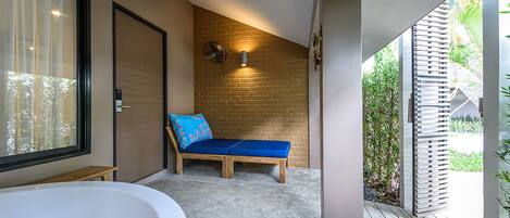 A modern bathroom with a large bathtub, a wooden bench with a blue cushion, and a brick wall.