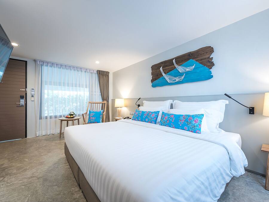 Una habitación de hotel moderna con una cama grande, una puerta de madera, una mesita con una silla y un adorno en la pared.