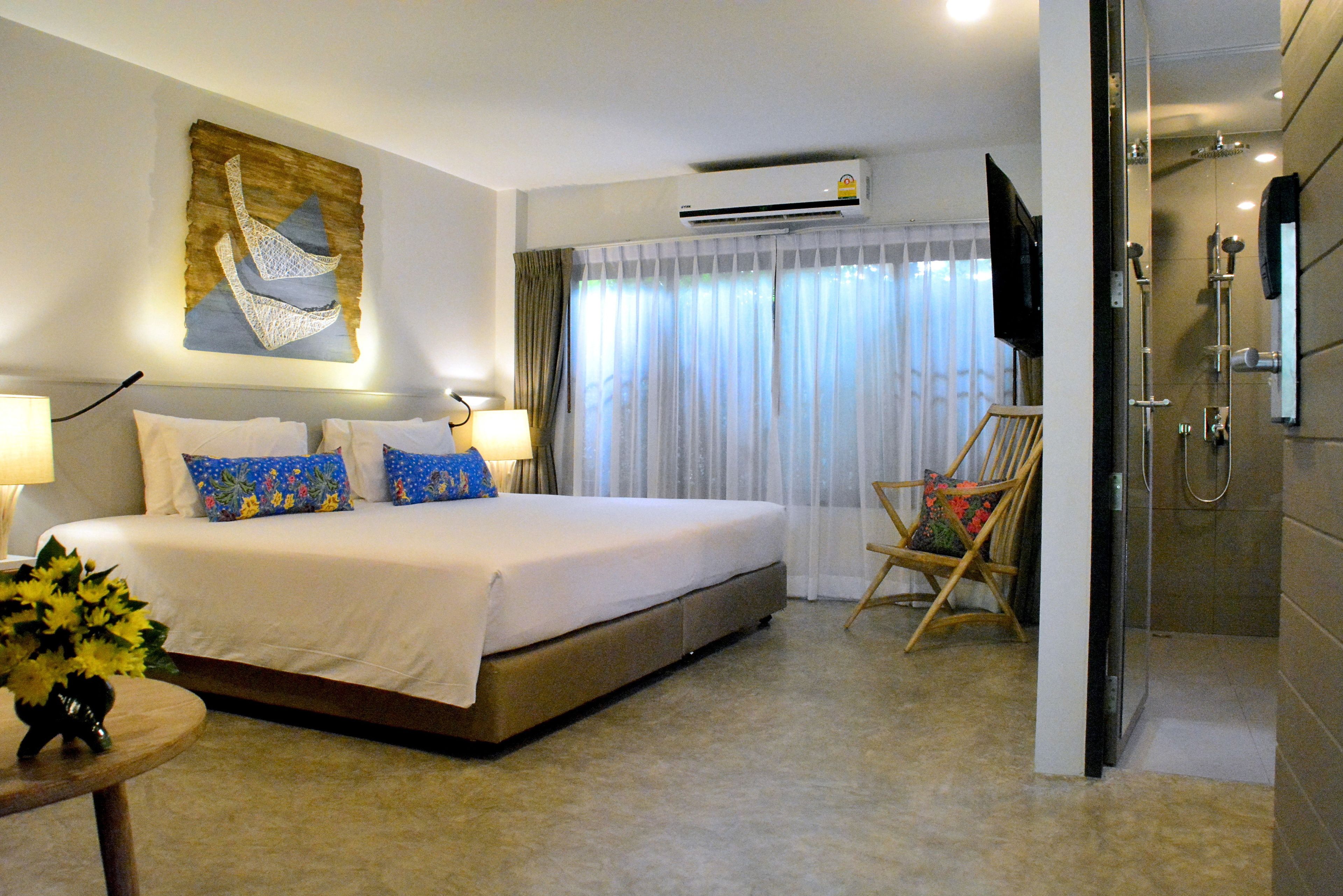 Una habitación de hotel con una cama grande, una silla, un televisor y un equipo de aire acondicionado.