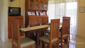 A dining area with a glass table, wooden chairs, a television on a cabinet, and a window with sheer curtains. - Oasi Fiore Bed and Breakfast (Dauis)