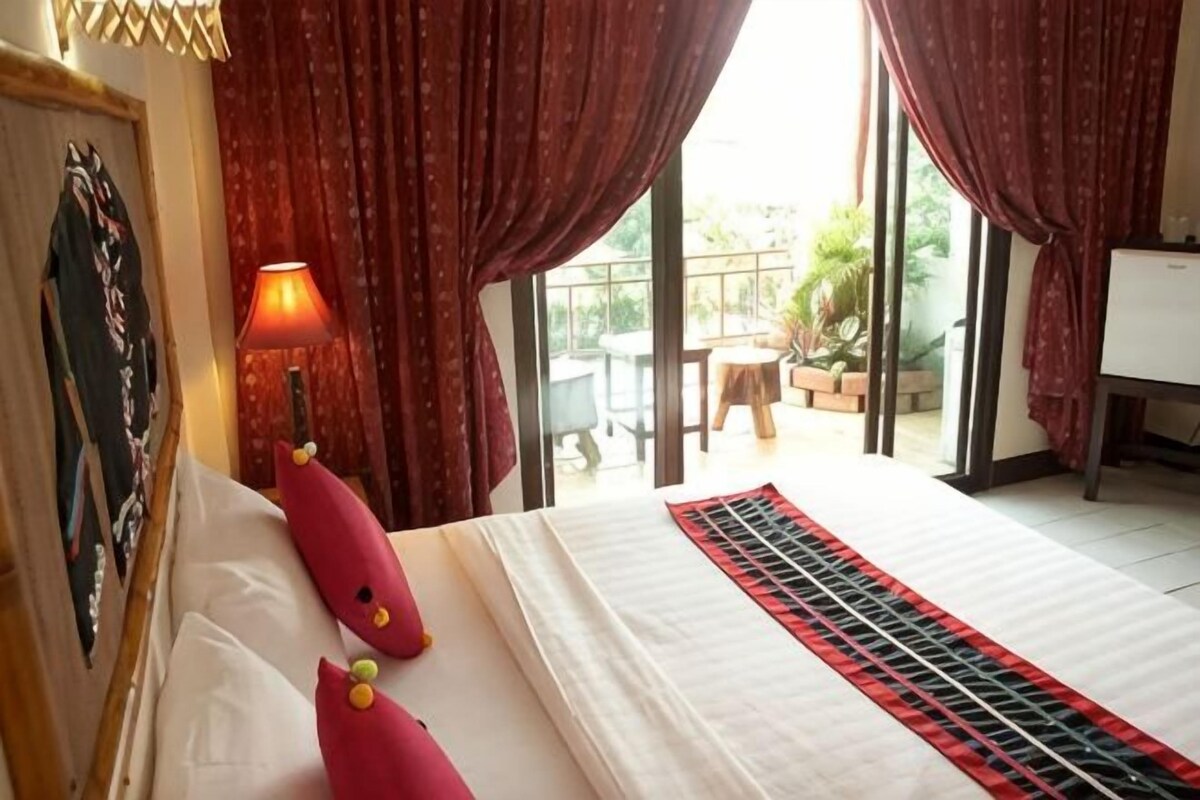 A hotel room with a bed, curtains, a lamp, and a view of the outdoors.