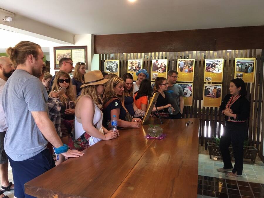A group of people gathered around a wooden bar in a room with a tiled floor and a wooden partition with framed pictures.