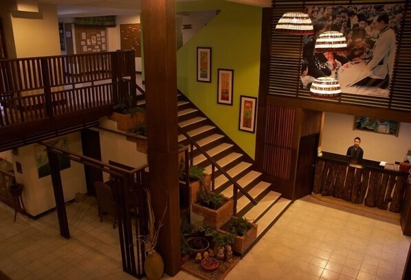 Vestíbulo de hotel con escalera, barandillas de madera y un mostrador de recepción.