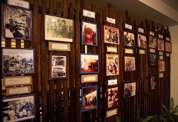 A wall with framed photographs and plaques, each labeled with a year, indicating a historical timeline. - Phumanee Lahu Home Hotel (Fang)