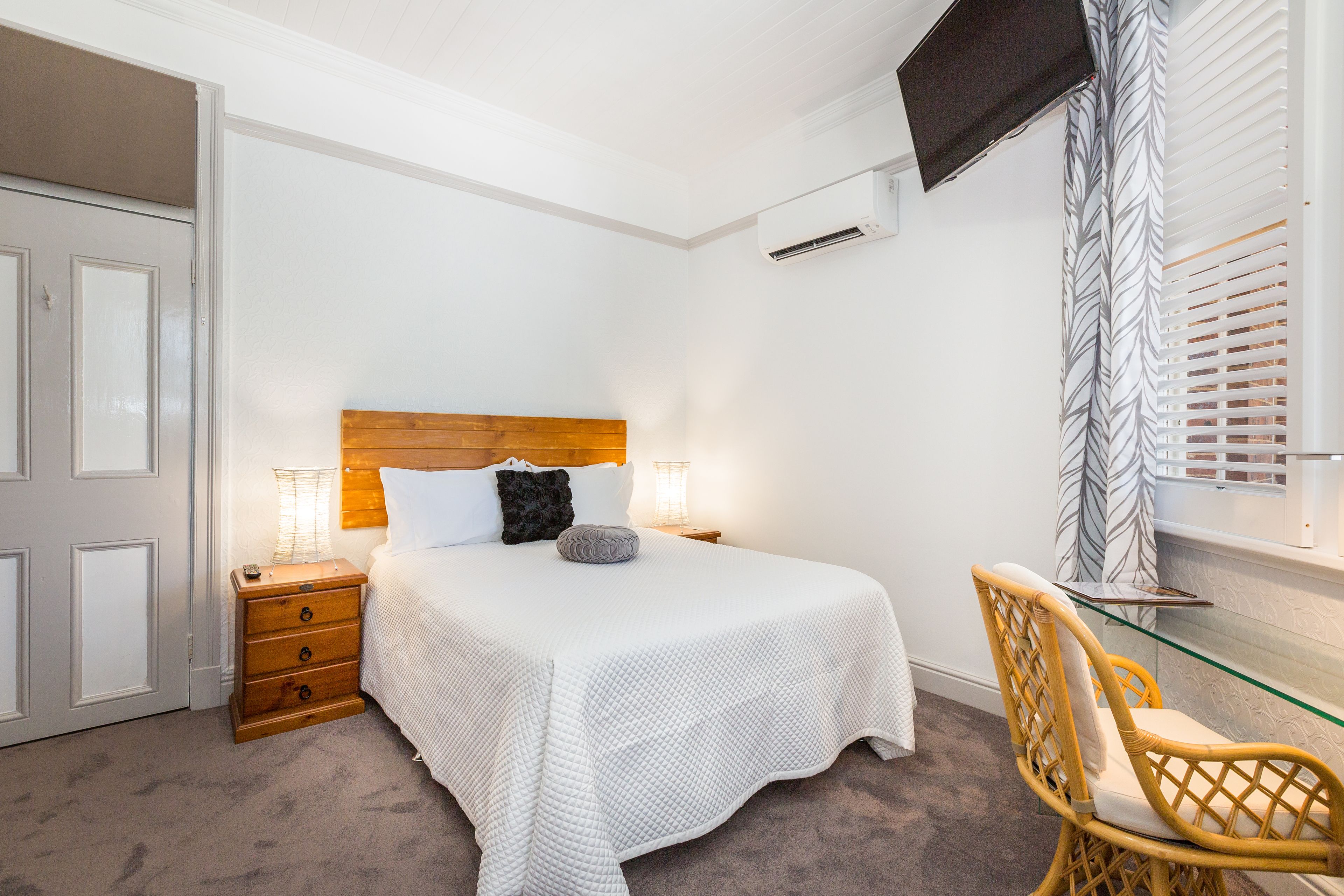 Un dormitorio con cama, mesita de noche, lámpara, sillón y televisor montado en la pared.