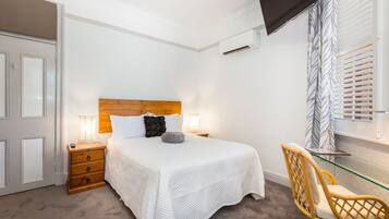 Un dormitorio con cama, mesita de noche, lámpara, sillón y televisor montado en la pared.