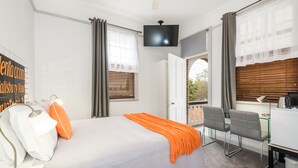 Una habitación de hotel con cama, escritorio, silla, televisor y ventana con persianas.